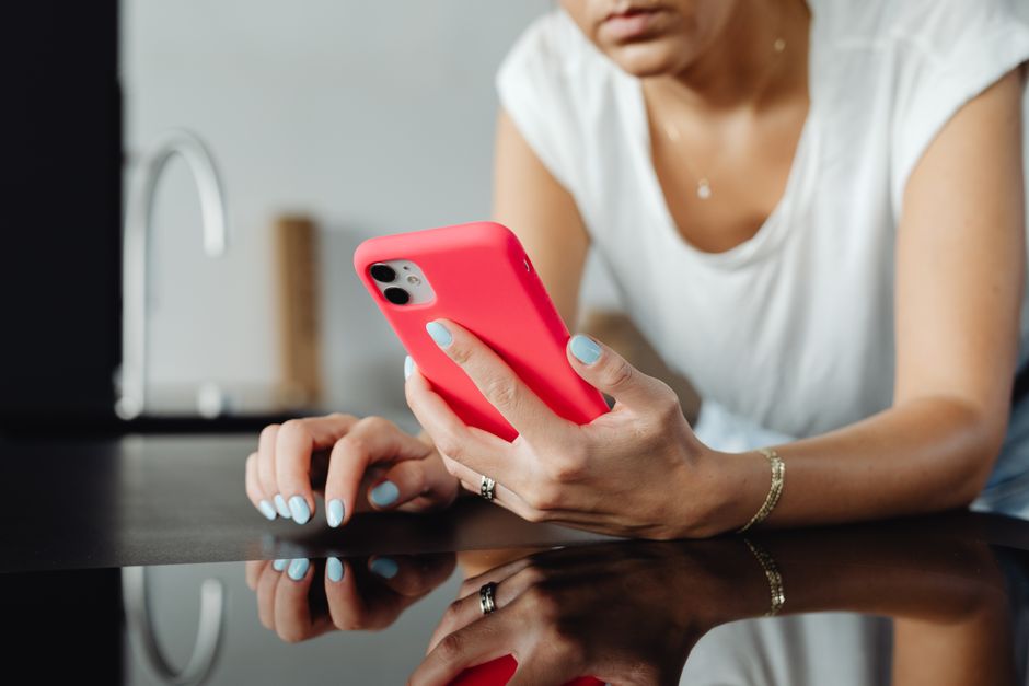 Close-up of a woman holding a smartphone with a pink case, showcasing nail art.